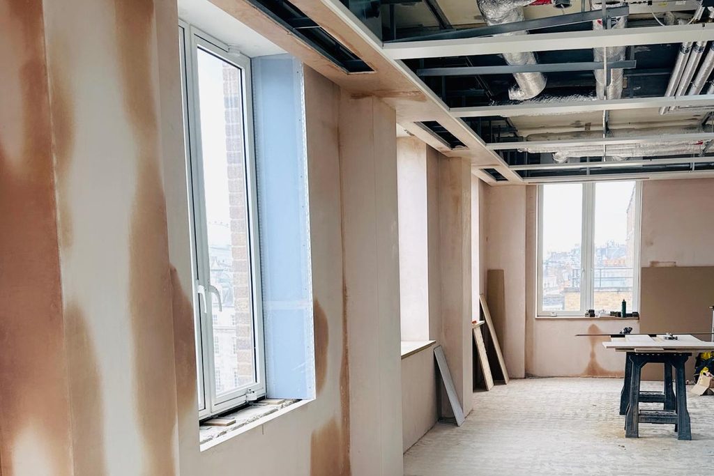 Plastered partitions and window reveals through a commercial floor, with an exposed-services ceiling zone. Photographed during finishing.
